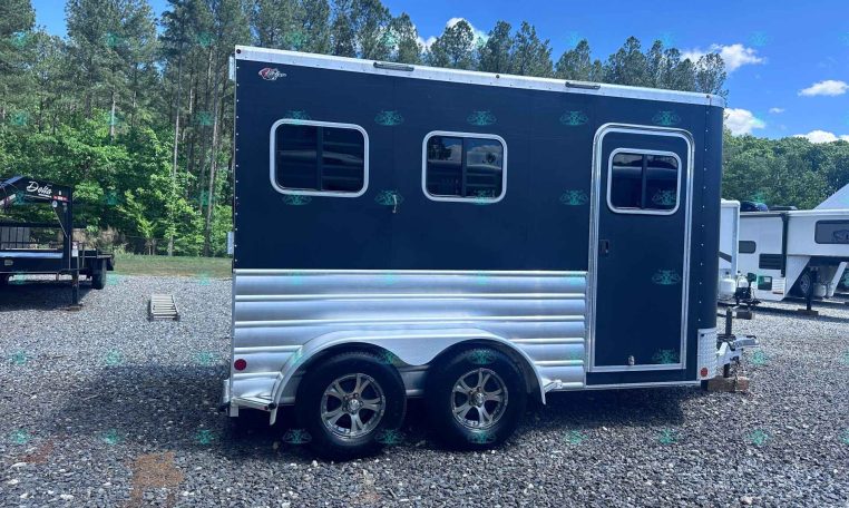 Dark blue travel trailer with two rectangular windows and a side door, parked on gravel with trees in the background.