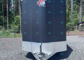 Enclosed gray cargo trailer with a diamond-plate front parked on a gravel lot among trees, ready to tow.