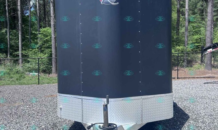 Enclosed gray cargo trailer with a diamond-plate front parked on a gravel lot among trees, ready to tow.