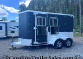 Dark blue horse trailer with two barred windows and aluminum trim, on a gravel lot with trees in the background.