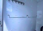 Interior of a white utility trailer with a row of hooks on a metal rail along the wall and a curved pipe along the base wall.