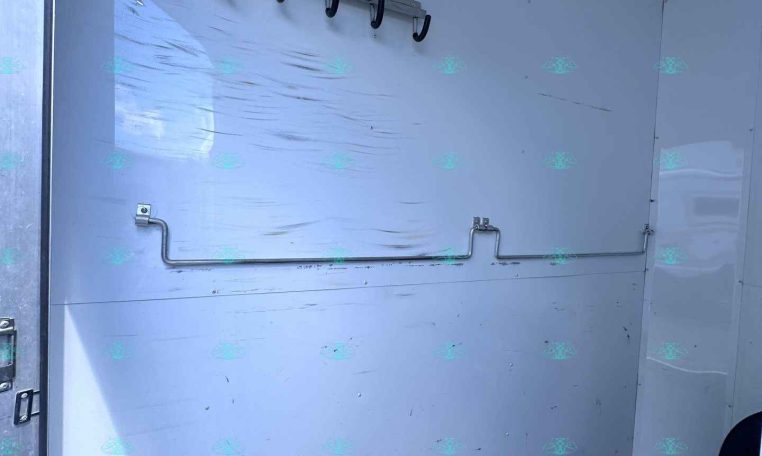 Interior of a white utility trailer with a row of hooks on a metal rail along the wall and a curved pipe along the base wall.