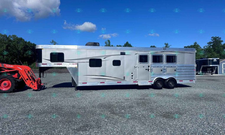 Silver multi-compartment trailer parked on a gravel lot under a blue sky with clouds; red tractor on the left and trees in the background.