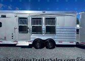 Silver horse trailer with three stall doors, barred windows, and chrome trim sits on gravel under a clear blue sky.