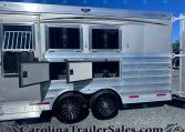Side view of a shiny silver Merhow horse trailer with open storage compartments and windows behind a clear blue sky.