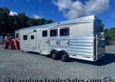 Silver Merhow horse trailer with multiple windows and side storage bays on a gravel lot under a blue sky.