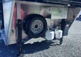 Open storage compartment of a utility trailer showing a mounted spare tire and propane tanks.
