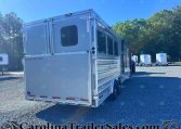 Silver Merhow horse trailer parked on a gravel lot with trees in the background and other trailers in the distance under a clear blue sky