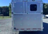 Rear view of a white Merhow trailer with a rounded window, parked on a gravel lot under a clear blue sky.
