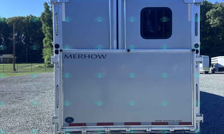 Rear view of a white Merhow trailer with a rounded window, parked on a gravel lot under a clear blue sky.