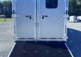 Rear of a silver cargo trailer with double doors, a small window on the right door, and a lowered loading ramp on a gravel lot.
