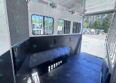 Interior of a horse trailer with padded walls, ventilation windows, and a tack area along the side, ready for loading horses outside.