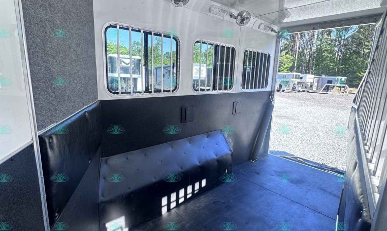 Interior of a horse trailer with padded walls, ventilation windows, and a tack area along the side, ready for loading horses outside.