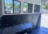 Interior of a white horse trailer with barred windows, ceiling fans, and ribbed walls, seen from the living area side.