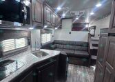 Interior of a modern RV kitchen and living area with dark cabinetry, marble-like counters, stainless steel appliances, and a gray sofa.