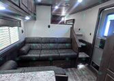 Interior of a compact RV living area with a dark leather sofa, overhead cabinets, and a kitchen counter to the right; bright ceiling lights and vents above.