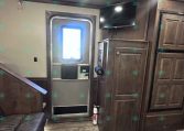 Interior of a wood-loaded trailer living area with a mounted TV, entry door, tall cabinets, and a fire extinguisher nearby.