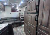 Interior of a modern RV with dark wood cabinets, a gray leather sofa, and a tall double-door refrigerator, view from the kitchen area.