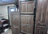 Tall dark-wood RV kitchen cabinet area with a built-in double-door refrigerator (Dometic) and surrounding cabinetry.