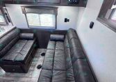 Dark wood cabinets above a black leather L-shaped sofa in an RV living area, with a window and blinds.