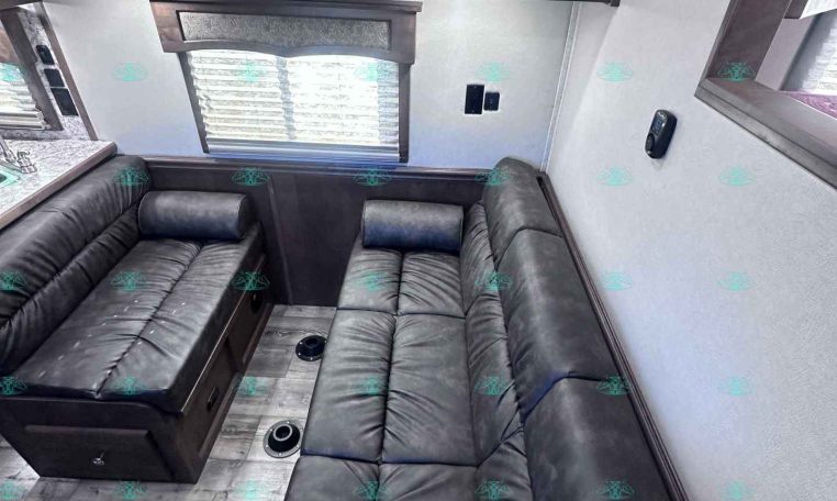 Dark wood cabinets above a black leather L-shaped sofa in an RV living area, with a window and blinds.