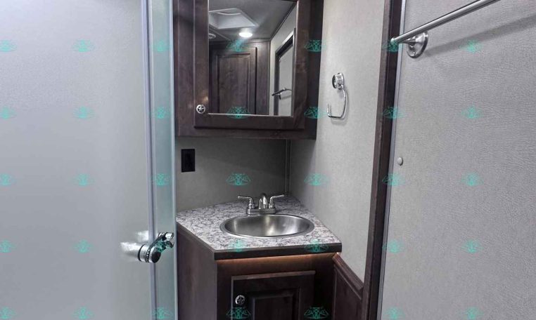 Small trailer bathroom with a dark wood vanity, granite countertop, round stainless sink, and a mirrored cabinet above.