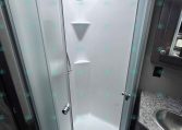 Curved glass shower enclosure in a compact RV bathroom with a white acrylic wall surround.
