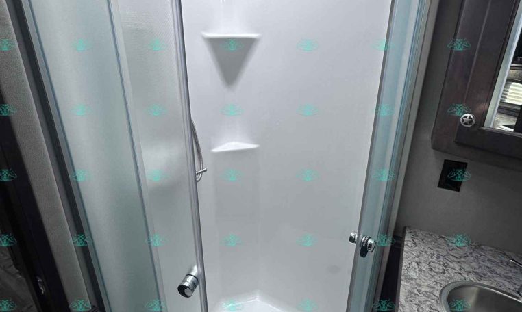 Curved glass shower enclosure in a compact RV bathroom with a white acrylic wall surround.