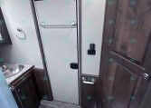 Small RV bathroom with a gray doorway, towel bar, and a toilet next to dark wood cabinet panels.