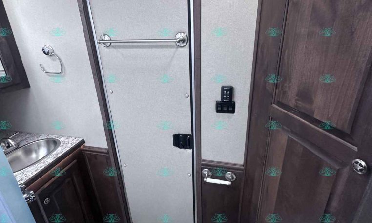 Small RV bathroom with a gray doorway, towel bar, and a toilet next to dark wood cabinet panels.
