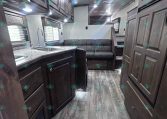 Interior of a modern RV kitchen and living area with dark wood cabinets, marble counters, stainless sink, and a grey sofa at the back