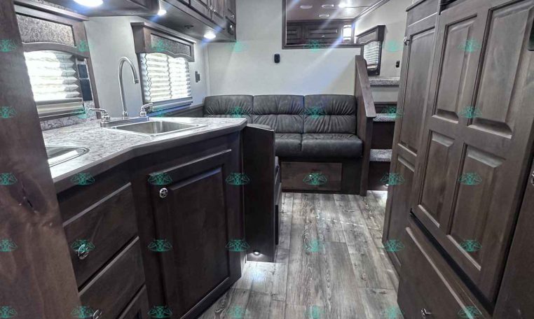 Interior of a modern RV kitchen and living area with dark wood cabinets, marble counters, stainless sink, and a grey sofa at the back