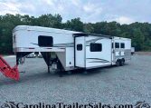 White fifth-wheel RV with an extended slide-out parked on a gravel lot, with a tree line in the background.