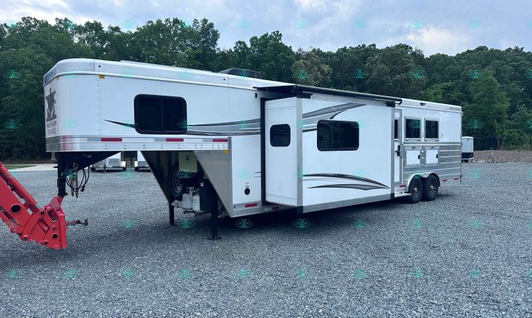 White fifth-wheel RV with an extended slide-out parked on a gravel lot, with a tree line in the background.