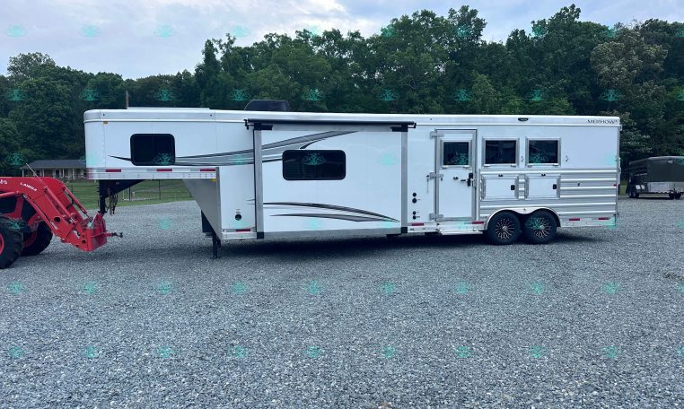 White horse trailer with windows parked on a gravel lot, with a red tractor attachment on the left and green trees in the background.
