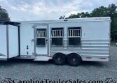 Side view of a silver Merhow horse trailer with barred windows, two axles, and a gravel lot in front of a treeline and cloudy sky.