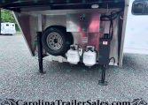 Open trailer storage area with a mounted spare tire, two propane tanks, hoses, and a metal storage box visible inside the compartment.