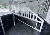 Interior of a white horse trailer with metal stalls and a divider, black cushioned walls, and windows on the sides