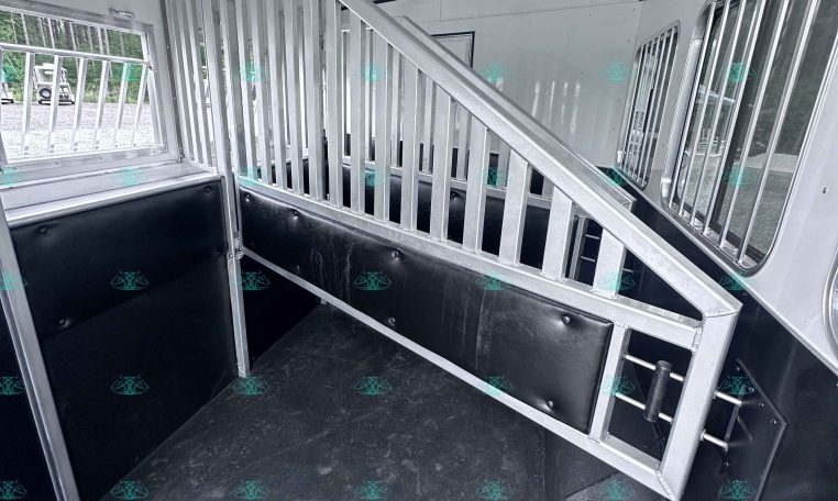 Interior of a white horse trailer with metal stalls and a divider, black cushioned walls, and windows on the sides