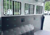 Interior of a white horse trailer showing barred windows, ceiling fans, and overhead lights.