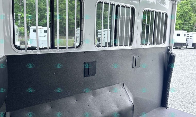Interior of a white horse trailer showing barred windows, ceiling fans, and overhead lights.