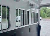 Interior of a silver trailer with ceiling fans, overhead lights, and barred windows along the side.
