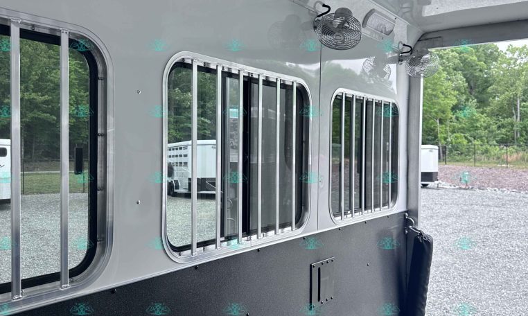 Interior of a silver trailer with ceiling fans, overhead lights, and barred windows along the side.