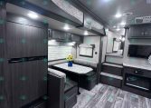 Interior of a dark wood RV with a U-shaped dinette, patterned cushions, and overhead storage cabinets under a light-gray ceiling.