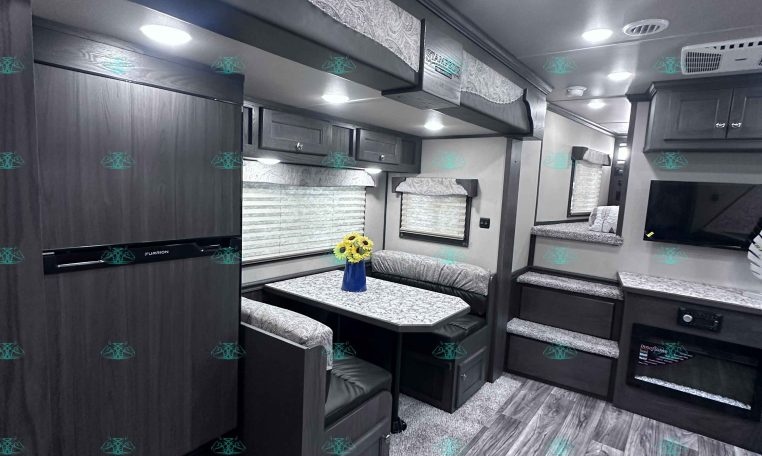 Interior of a dark wood RV with a U-shaped dinette, patterned cushions, and overhead storage cabinets under a light-gray ceiling.