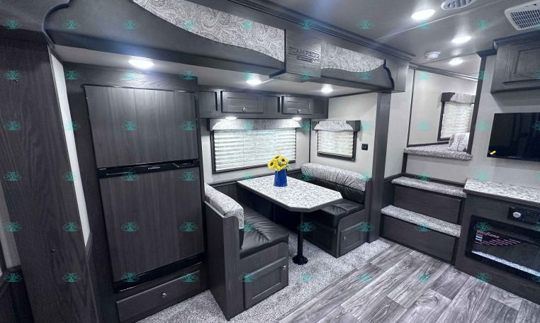 RV living area with dark wood cabinets, U-shaped dinette, and marble-patterned countertops; sunflowers on the table.