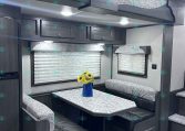 RV dining nook with dark wood booths, patterned cushions, and a marble-pattern table beneath overhead cabinets and a decorative valance without natural light sources visible