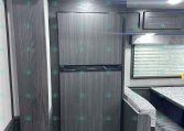 Interior of a dark wood RV kitchen with upper cabinets, a built-in Furrion oven, and a decorative ceiling pattern above.