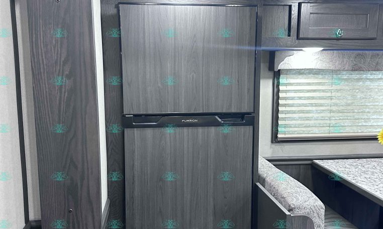 Interior of a dark wood RV kitchen with upper cabinets, a built-in Furrion oven, and a decorative ceiling pattern above.