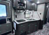 RV kitchen with dark wood cabinets, stainless microwave, stovetop, and double sink on a marble backsplash counter area